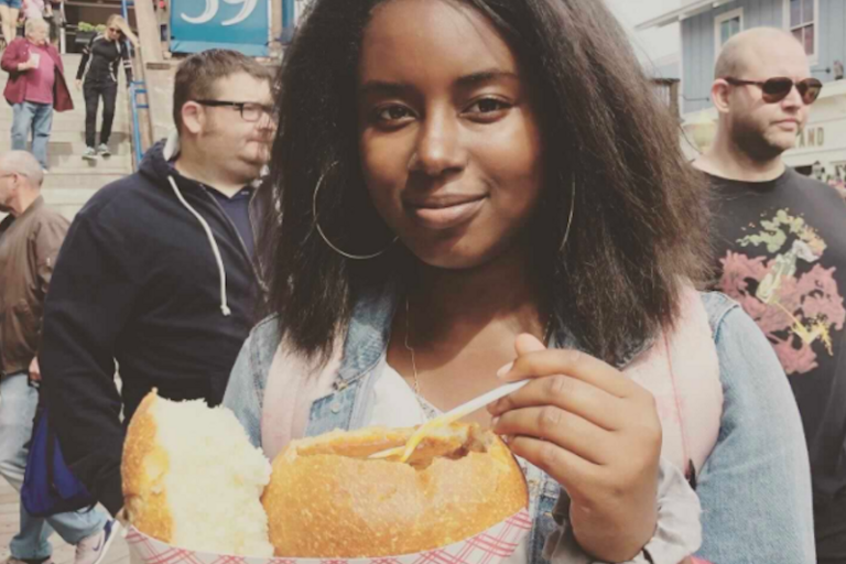 Photo of Danielle smiling and looking at the camera in casual attire eating from a bread bowl