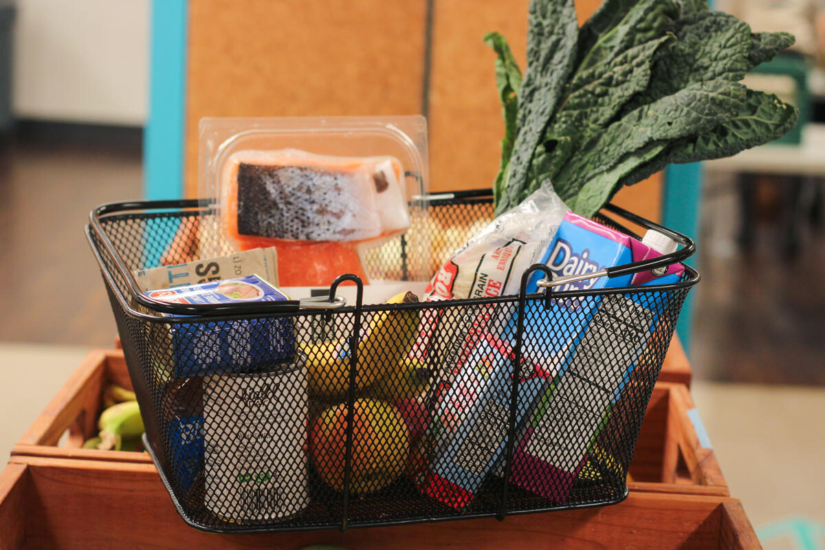 Photo of grocery basket filled with pantry items like juice, milk, frozen fish, canned goods, fruit